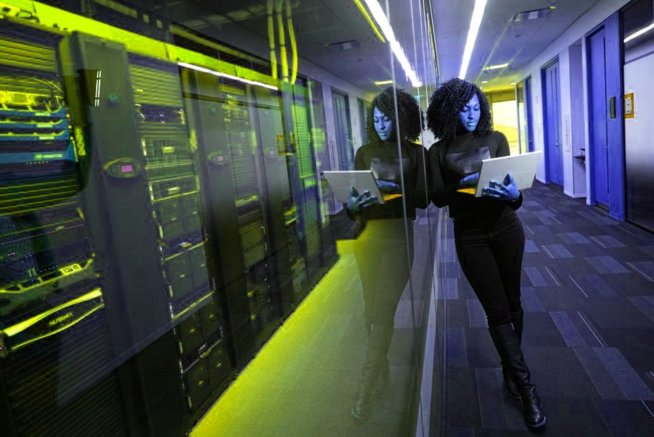 Femme sur un ordinateur portable dans un datacenter aux serveurs en miroir.